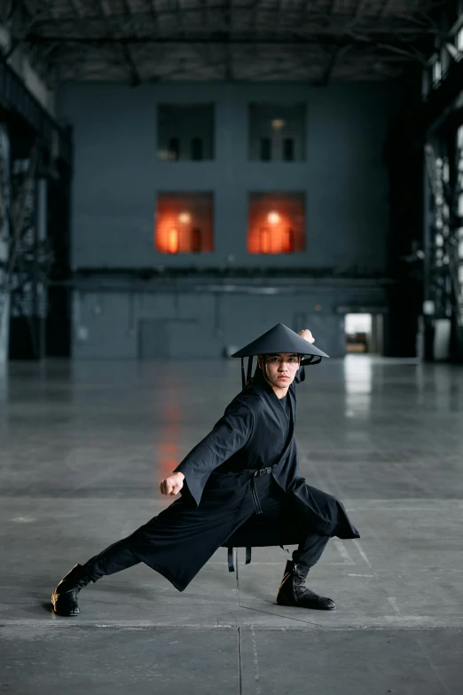 a person in a black outfit doing a trick, inspired by Ma Quan, black pointed hat, in a dojo, posing, reuben wu