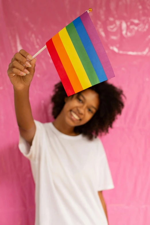 a young girl holding a rainbow flag in front of a pink wall, trending on pexels, black teenage girl, a still of a happy, holding a wooden staff, a handsome