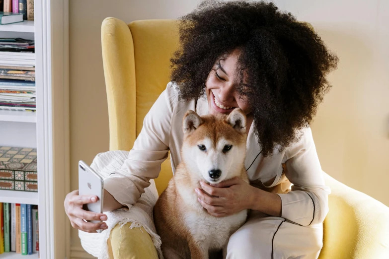 a woman sitting in a yellow chair holding a dog, trending on pexels, holding a very advance phone, shiba inu, hugging each other, photo of a black woman