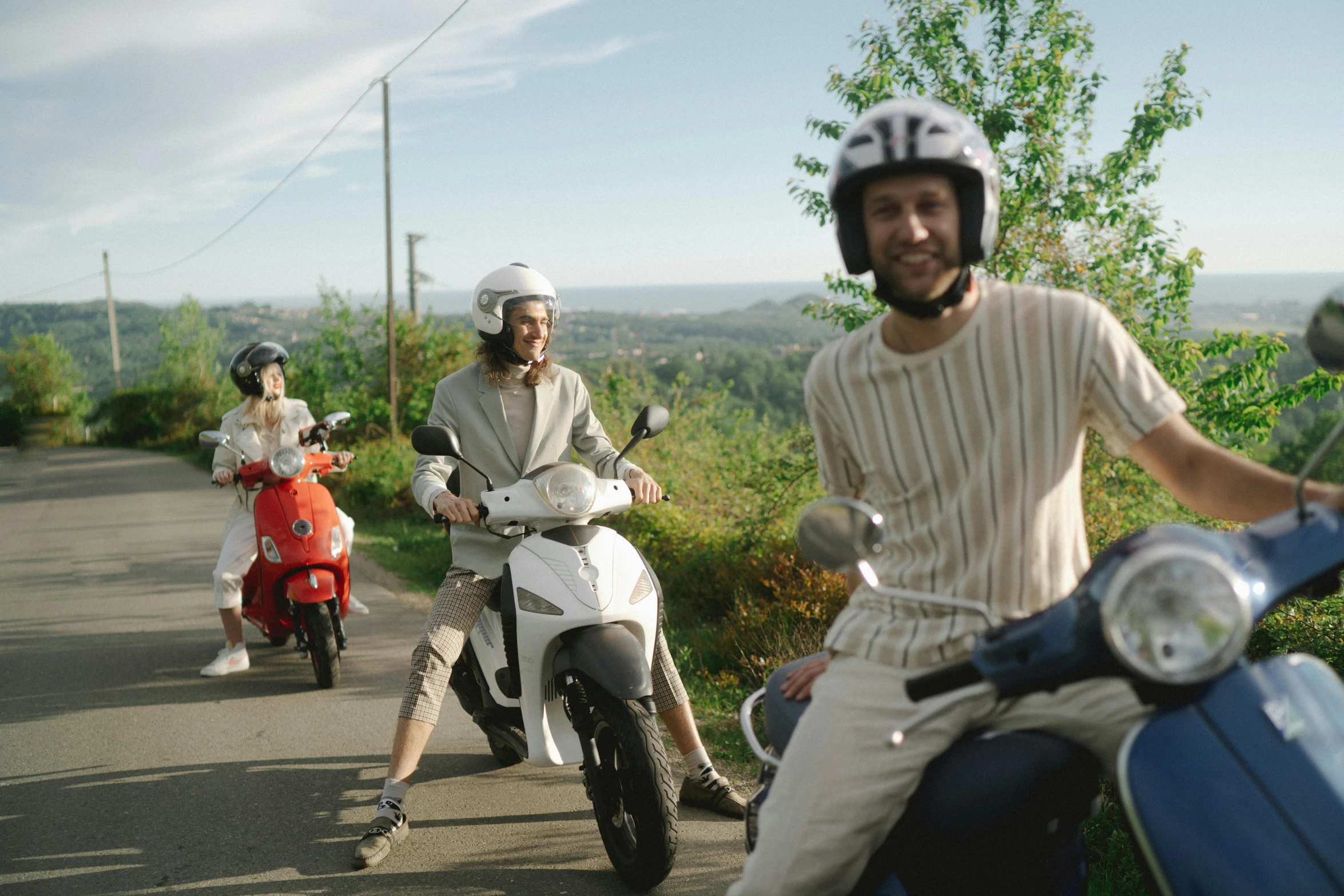 a group of people riding scooters down a road, in style of heikala, over the hills, still from l'estate, looking happy