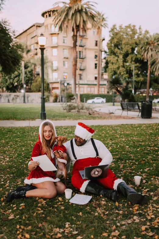 a couple of people that are sitting in the grass, wearing a santa hat, sitting on the ground, sydney sweeney, in a city square