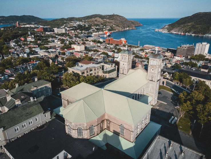 a large church sitting on top of a lush green hillside, renaissance, harbour in background, drone photograph, view from the streets, brown