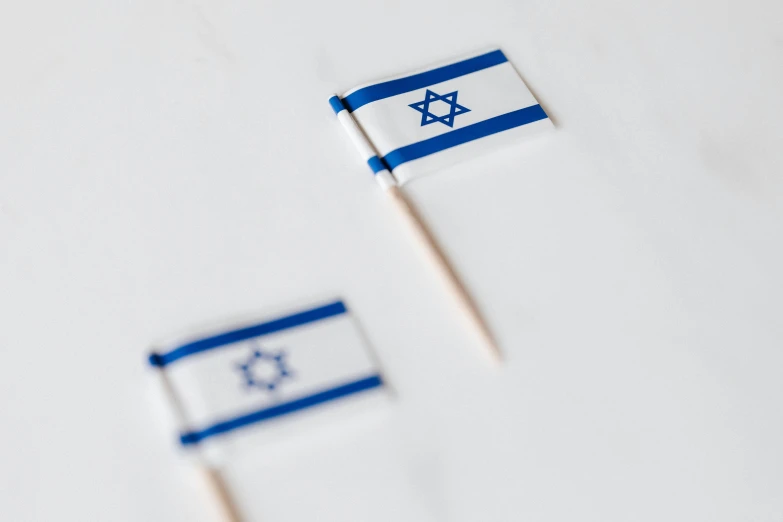 a couple of small flags sitting on top of a table, pexels, dau-al-set, israel, square, on white paper, wooden