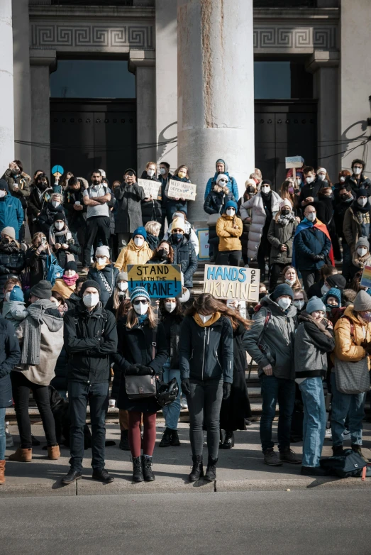 a large group of people standing in front of a building, masks, protest movement, thumbnail, quebec