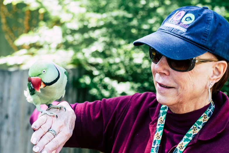 a close up of a person holding a bird, by Bernie D’Andrea, wearing sunglasses and a hat, lynn skordal, parrot, exploring