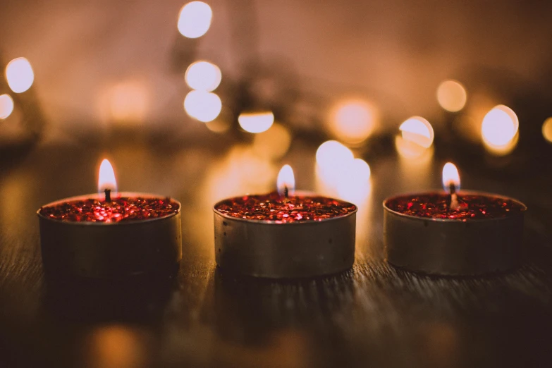 three lit candles sitting on top of a wooden table, by Emma Andijewska, trending on pexels, crimson themed, glitter, in a row, tranquil