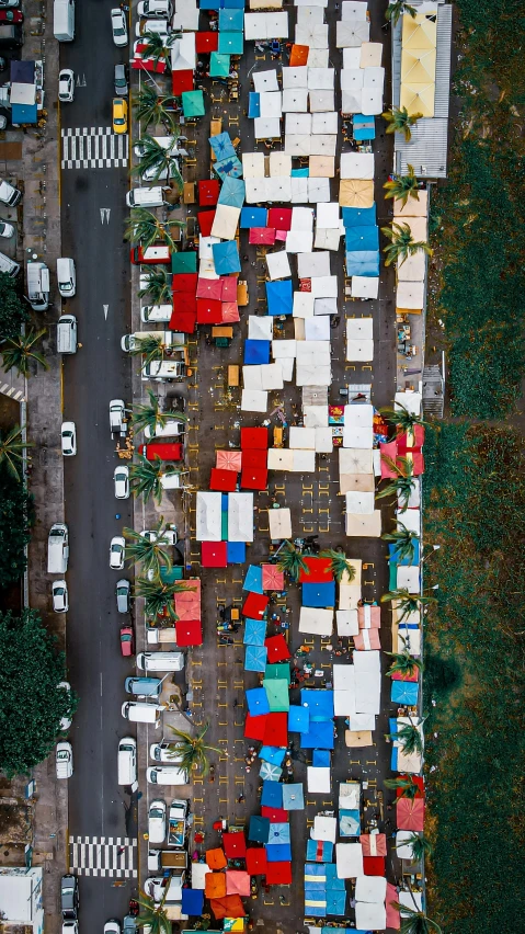a street filled with lots of traffic next to a forest, an album cover, by Samuel Scott, trending on unsplash, tents, color aerial photo drone, puerto rico, red blue and gold color scheme