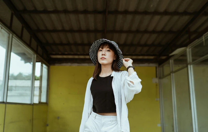 a woman standing in a room with a hat on, pexels contest winner, young asian girl, cropped shirt with jacket, white straw flat brimmed hat, in front of a garage