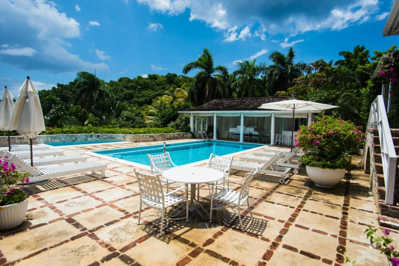 a patio with a table and chairs next to a swimming pool, jamaican vibe, critically acclaimed, mansion, thumbnail