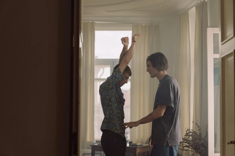 a couple of men standing next to each other in a living room, by Emma Andijewska, happening, raising an arm, perfectly lit. movie still, hammershøi, greeting hand on head