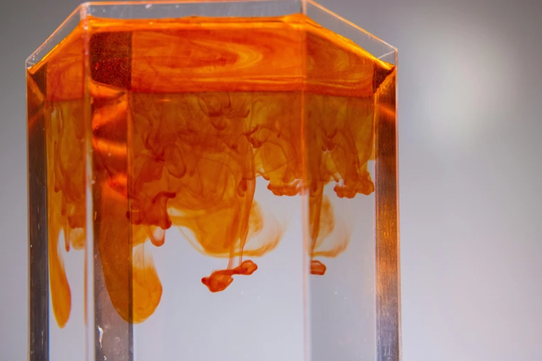 a close up of a vase with liquid in it, an abstract sculpture, inspired by Hugo Kārlis Grotuss, unsplash, process art, orange color, translucent cube, underwater ink, trending on dezeen