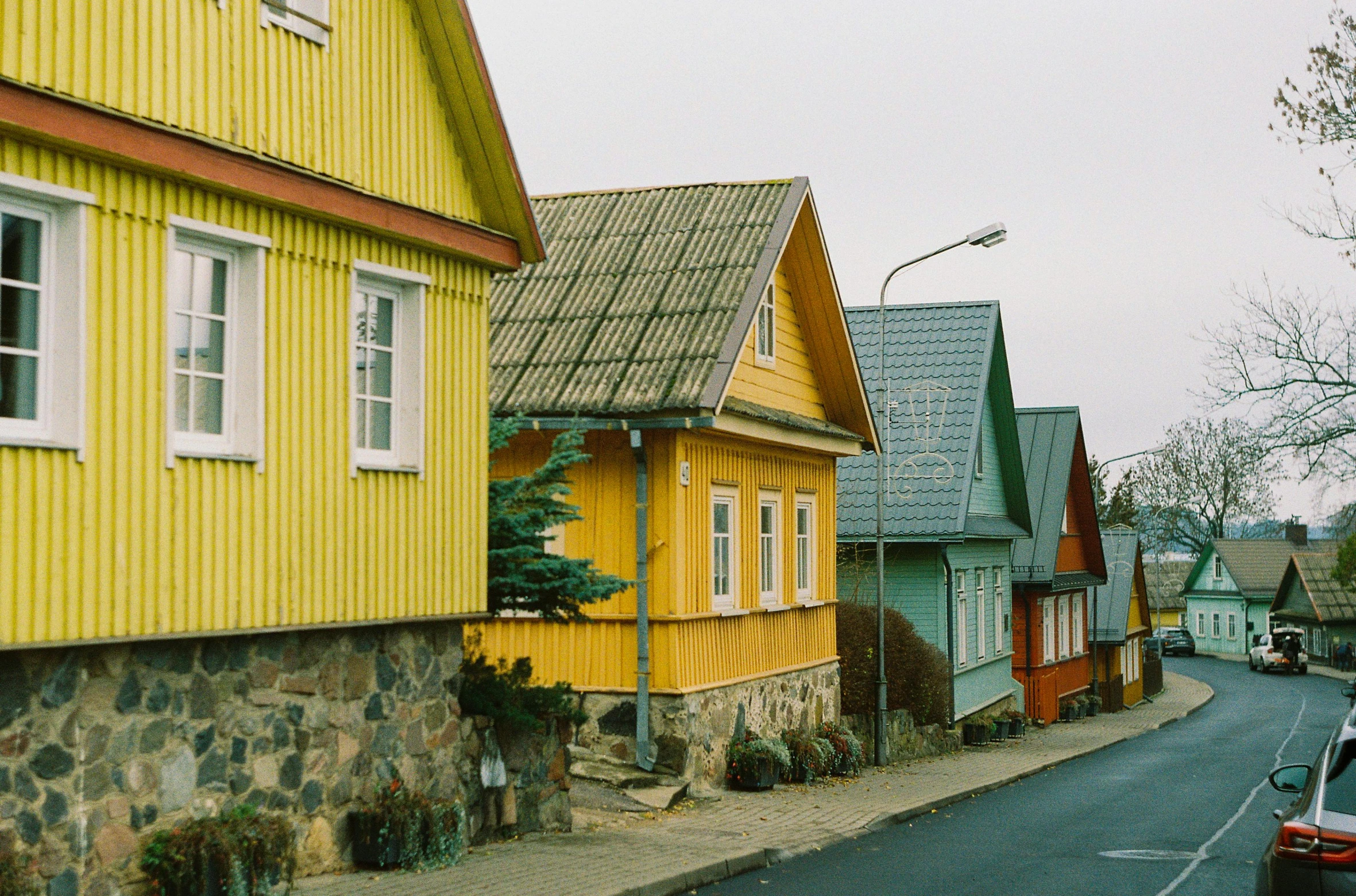 a row of houses on the side of a road, a colorized photo, by Attila Meszlenyi, unsplash contest winner, hyperrealism, yellows, wooden houses, zdzislaw beksinsk, taken in the late 2000s