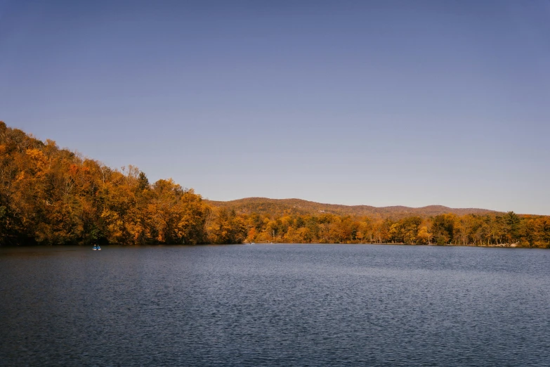 a large body of water surrounded by trees, a photo, trending on unsplash, hudson river school, blue and orange tones, digital image, color ( sony a 7 r iv, yellow