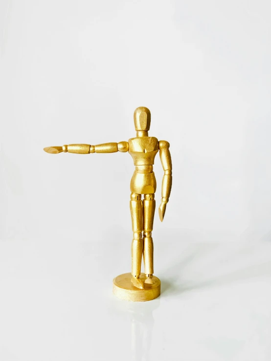 a gold figurine standing on a white surface, by Gavin Hamilton, art deco bowling alley, hand gesture, wooden, hero prop