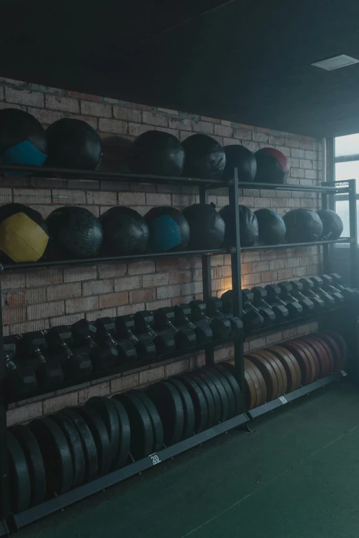 a man standing in front of a rack full of dumbs, by Alejandro Obregón, unsplash, local gym, somber lighting, some spherical, slate