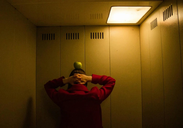 a man standing in a room with a green apple on his head, inspired by Elsa Bleda, unsplash, process art, lockers, upside down stranger things, red cap, ignant