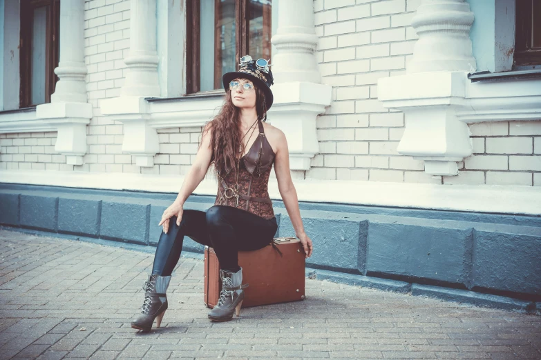 a woman sitting on a suitcase in front of a building, by Maksimilijan Vanka, pexels contest winner, art nouveau, steampunk hat, concert, wearing a camisole and boots, dasha taran
