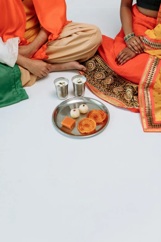 a man and a woman sitting next to each other, samikshavad, offering a plate of food, orange and white color scheme, stainless steel, - 9