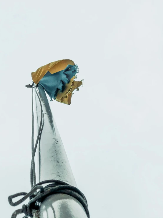 a close up of a metal object with a butterfly on it, a statue, by Ryan Pancoast, unsplash, new sculpture, yellow and cyan color palette, standing on the mast, during a storm, blue torn fabric