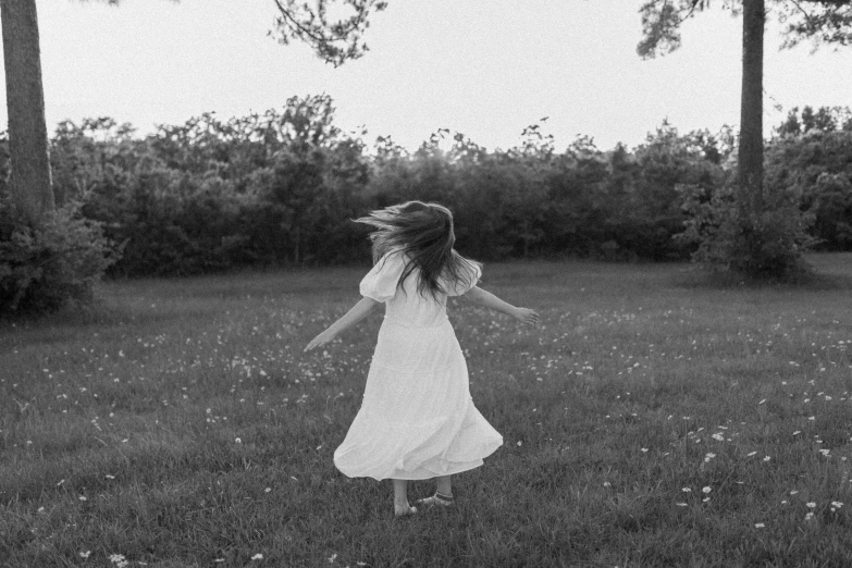a black and white photo of a girl in a field, inspired by Nell Dorr, pexels, renaissance, girl in white dress dancing, cottagecore hippie, weightless, low quality footage