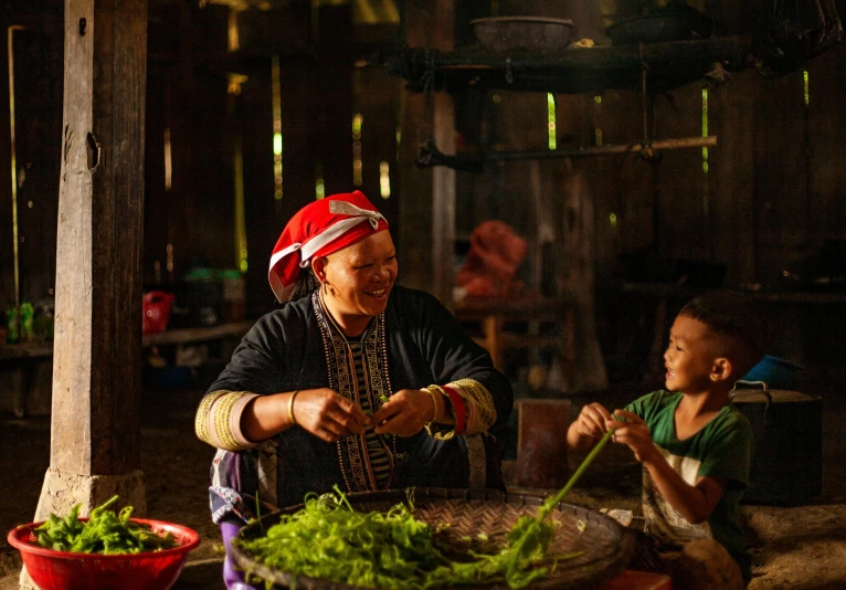 a woman sitting in front of a table filled with food, by Dan Content, pexels contest winner, tai traditional bronze headdress, with a kid, ja mong, thumbnail