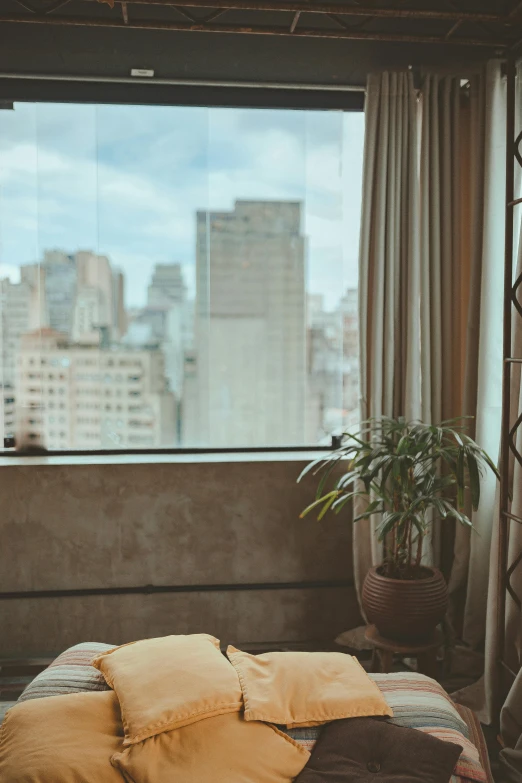 a bed sitting in a bedroom next to a window, by Elsa Bleda, unsplash, modernism, window with rio de janeiro view, skyscrapers with greenery, relaxing on the couch, grainy vintage