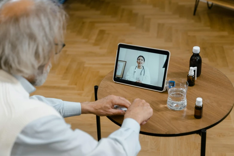 a man sitting at a table in front of a tablet computer, doctors mirror, victoria siemer, thumbnail, long distance shot