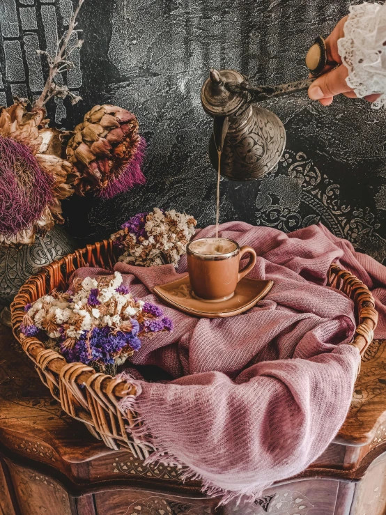 a basket of flowers and a cup of coffee on a table, a picture, by Lucia Peka, process art, brewing potion in witch hut, brown and pink color scheme, promo image, made of dried flowers