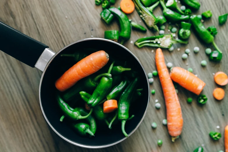 a pan filled with carrots and peas on top of a wooden table, by Emma Andijewska, pexels contest winner, process art, mortar and pestle, oprah okra winfrey sentient veg, green steam rising from soup, a super-smart