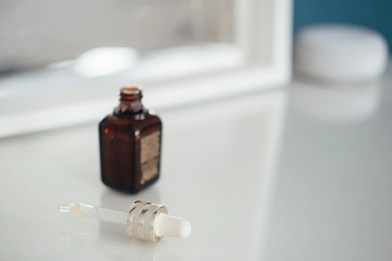 a close up of a bottle of liquid on a table, inspired by Elsa Bleda, unsplash, skin care, syringe, brown, white