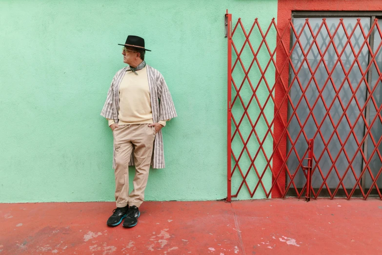 a man standing in front of a green wall, an album cover, inspired by Joseph Beuys, de stijl, hispanic, an elderly, stripes, clothed in ancient street wear