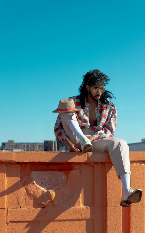 a man sitting on top of a brick wall, by Pamela Ascherson, pexels, a black man with long curly hair, moonwalker photo, slide show, on rooftop