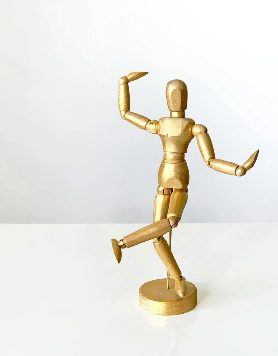 a gold figurine sitting on top of a white table, dancing a jig, 2019 trending photo, made of wood, full body hero