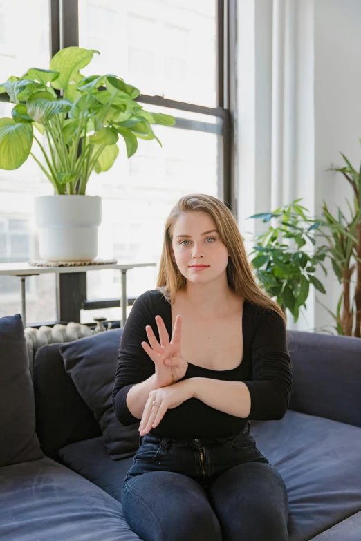 a woman sitting on top of a blue couch, by Sara Saftleven, unsplash, visual art, wave a hand at the camera, sydney sweeney, on a white table, transplanted hand to head