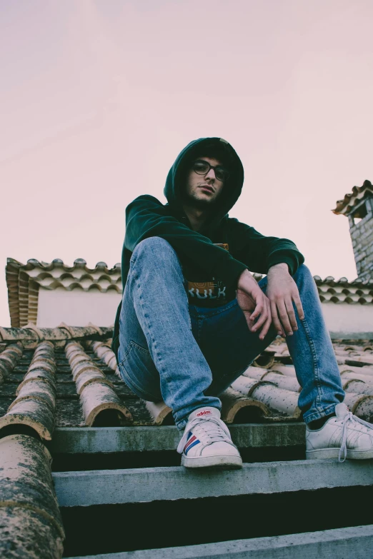 a man sitting on top of a set of stairs, an album cover, by Alexis Grimou, unsplash, aestheticism, wearing jeans and a black hoodie, roofs, looking the camera, sunfaded