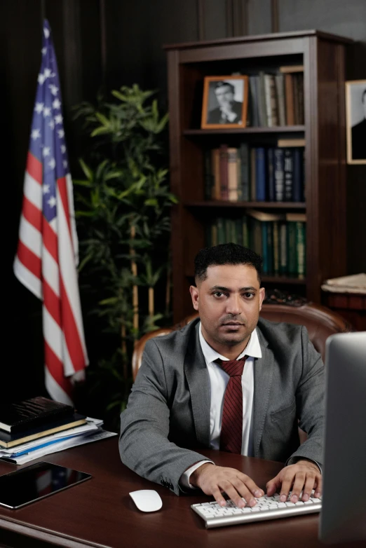 a man sitting at a desk in front of a computer, politics, riyahd cassiem, promo image, defense attorney