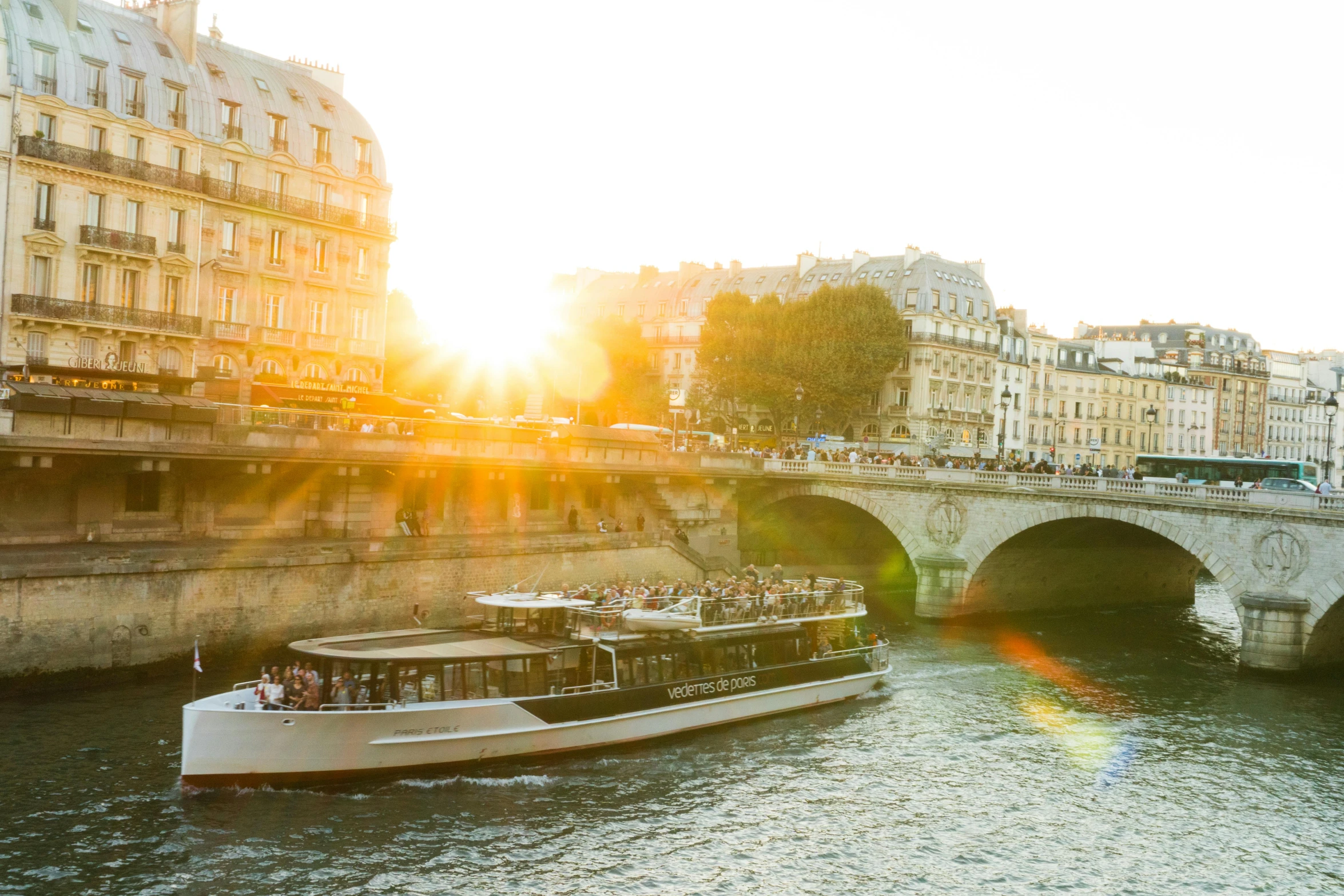 a boat traveling down a river next to a bridge, by Julia Pishtar, pexels contest winner, art nouveau, golden sunlight, paris hotel style, olafur eliasson, group photo