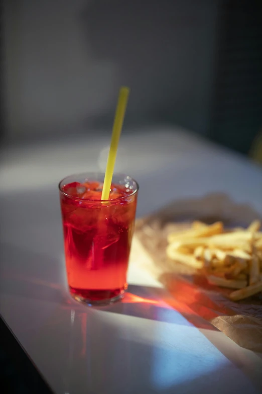 a drink sitting on top of a table next to french fries, by Nathalie Rattner, pexels, translucent neon, maroon red, lemonade, low iso