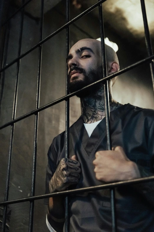 a man standing behind bars in a jail cell, a tattoo, inspired by James Bolivar Manson, trending on pexels, zayn malik, ( ( theatrical ) ), nipsey hussle, bald