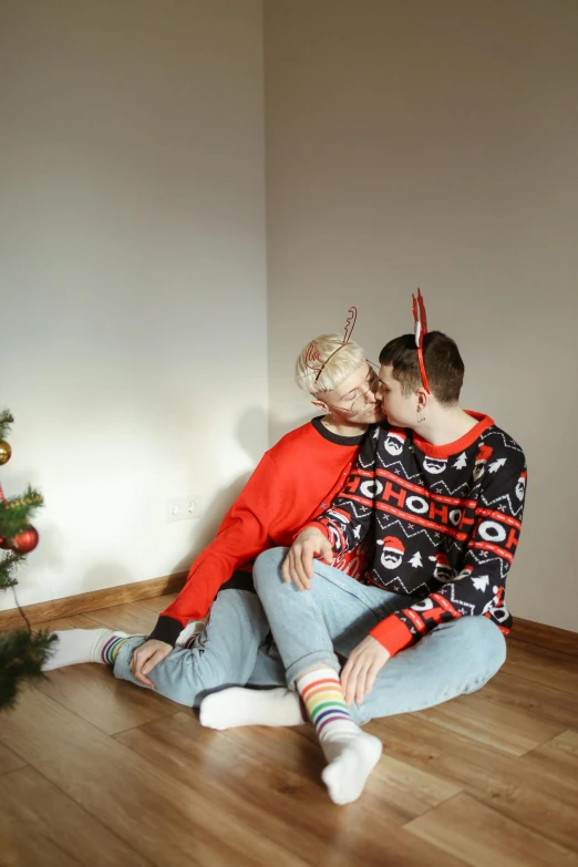 a man and woman sitting on the floor in front of a christmas tree, by Julia Pishtar, pexels, realism, lesbian kiss, wearing a sweater, genderless, 15081959 21121991 01012000 4k