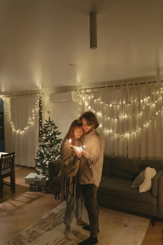 a man and a woman standing in a living room, by Liza Donnelly, pexels, light and space, christmas lights, cosy, decoration around the room, natural candle lighting