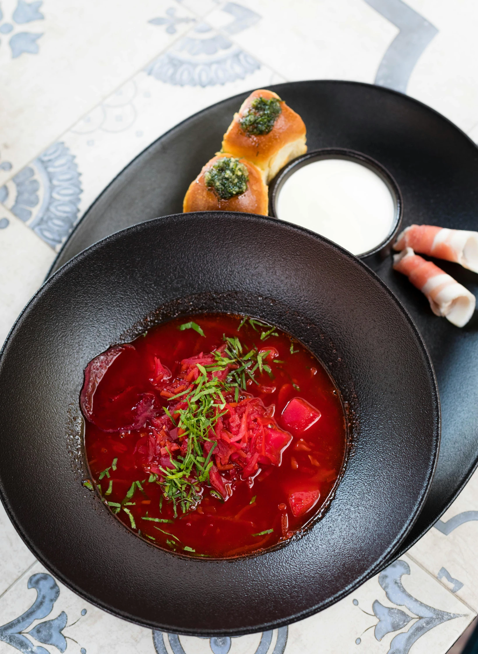 a bowl of soup sitting on top of a black plate, by Julia Pishtar, art nouveau, plate of borscht, chef table, prussian blue and venetian red, russian and japanese mix