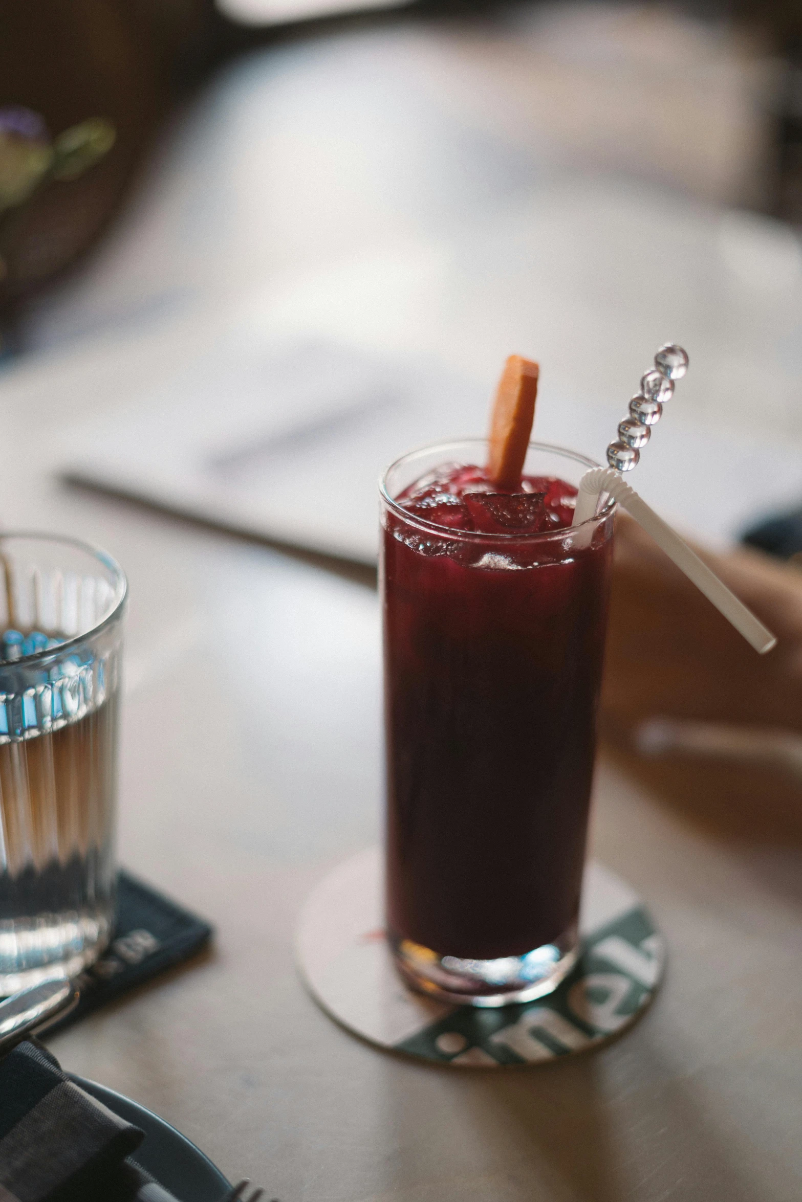 a glass of juice sitting on top of a wooden table, inspired by Richmond Barthé, maroon, with a straw, swedish, dessert