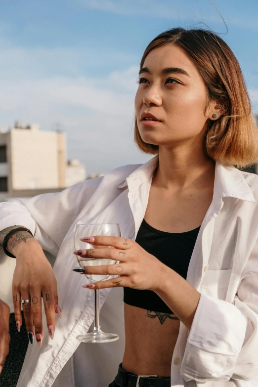 a woman sitting on a balcony holding a glass of wine, a portrait, inspired by Ruth Jên, trending on unsplash, aestheticism, lab coat and tee shirt, of taiwanese girl with tattoos, standing on rooftop, with a bob cut