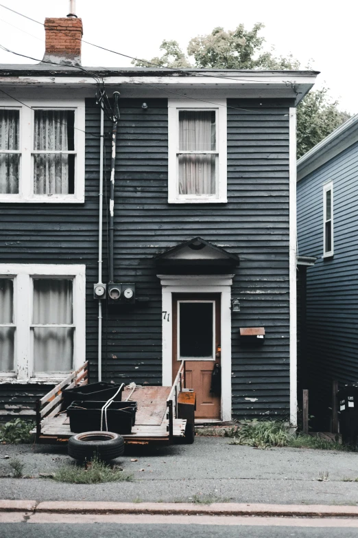 a black house sitting on the side of a road, by Carey Morris, pexels contest winner, maximalism, new england architecture, leaning on door, dingy city street, white plank siding