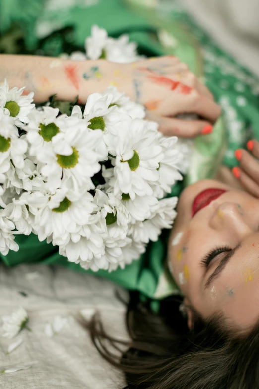 a woman laying on a bed holding a bunch of flowers, trending on unsplash, art photography, white facepaint, green and white, splatter paint, daisies