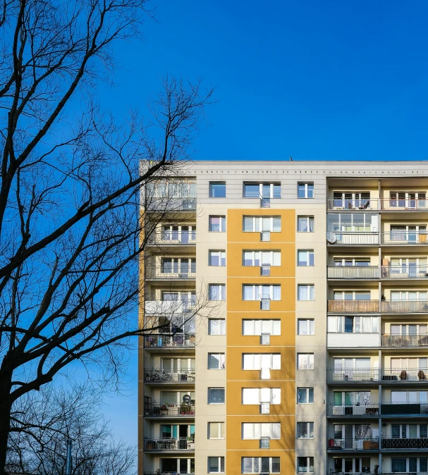 a tall building with lots of windows and balconies, by Kristian Zahrtmann, unsplash, bauhaus, a ghetto in germany, massive trees with warm windows, clear blue skies, getty images