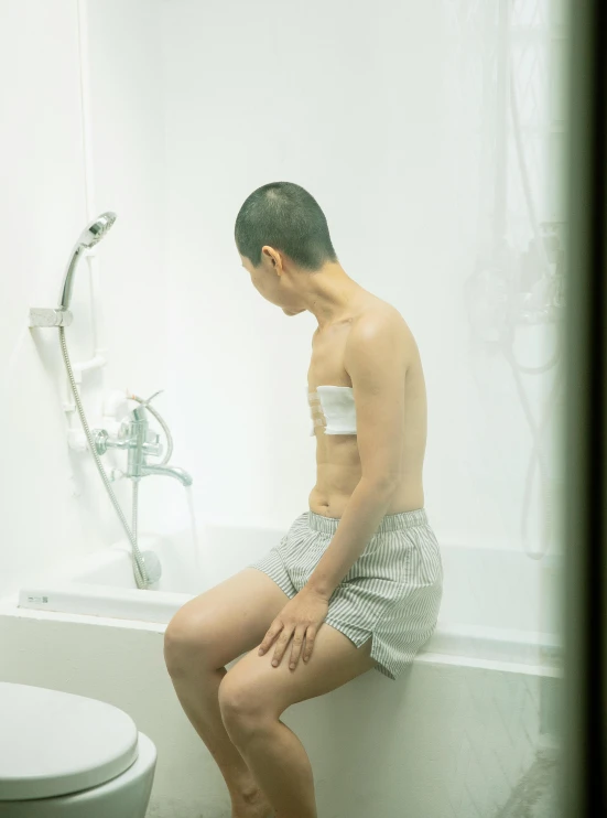 a man sitting on the edge of a bath tub, by Yanagawa Nobusada, unsplash, shin hanga, genderless, hospital room, transparent body, he is about 20 years old | short