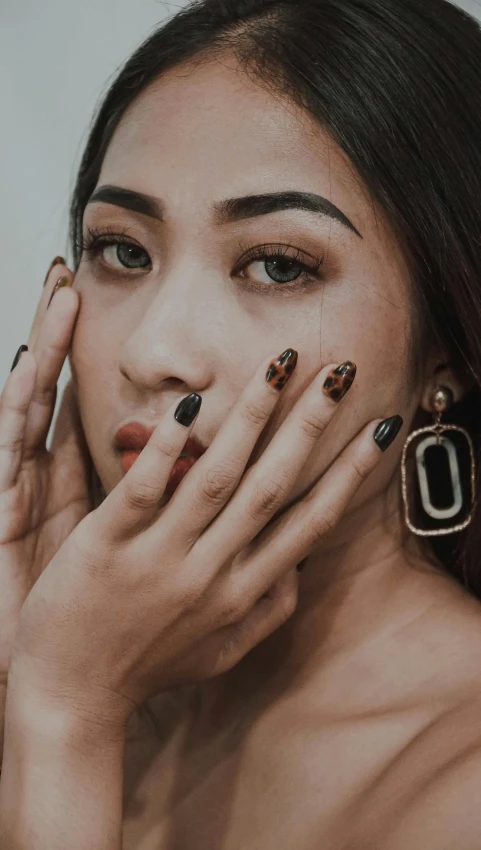 a woman holding her hands to her face, trending on pexels, hyperrealism, nail art, black and brown colors, media photo, batik