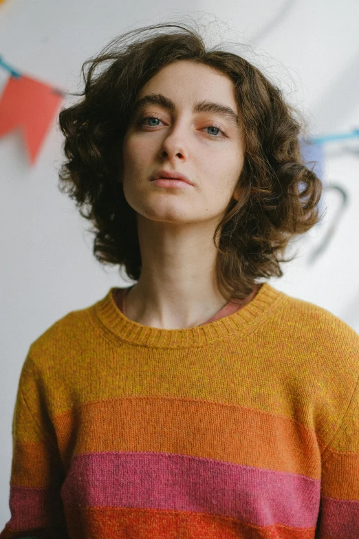 a woman standing in front of a white wall, wearing a sweater, adam ondra, orange yellow ethereal, portrait image